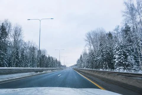 Empty winter road surrounded by snow covered forest during daytime. Cold season Stock Photos