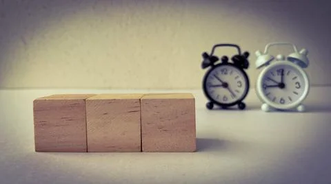 Empty wooden blocks with two blurred alarm clocks background. Copy space concept Foto stock