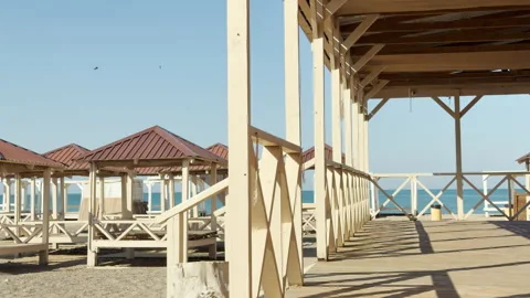 Empty Wooden Cabanas and Sun Deck Sit Peacefully Along a Calm Sunny Beach Stock Footage 334513441