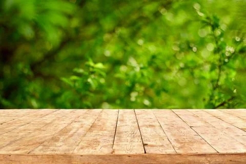 Empty wooden deck table with foliage bokeh background. Stock Photos