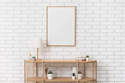Empty wooden frame on a white brick wall above a console table with home deco Stock Photos