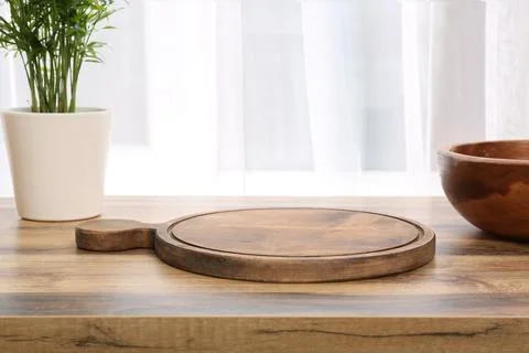 Empty wooden pizza board on rustic table with green plant and window light, k Stock Photos