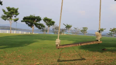 Empty wooden swing gently blown by the wind in the park Video stock 232845492