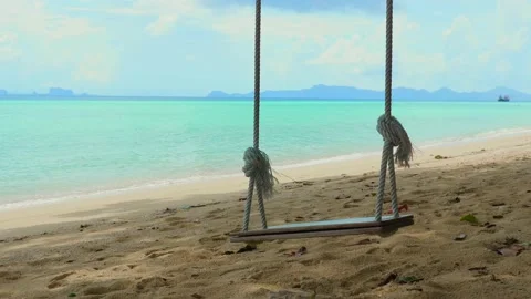 An empty wooden swing sways gently in breeze on a tropical beach Video stock 236937904