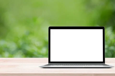 Empty wooden table with blank screen laptop on green blurred abstract background Stock Photos