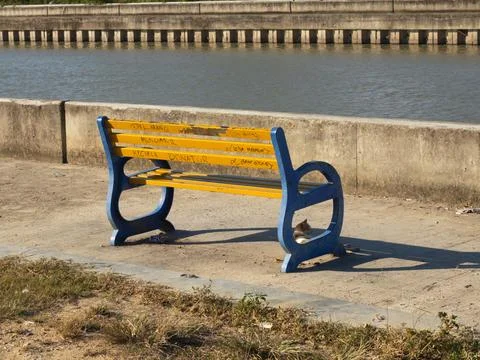 Empty Yellow and Blue Bench by a Canal on a Sunny Day Stock-Fotos
