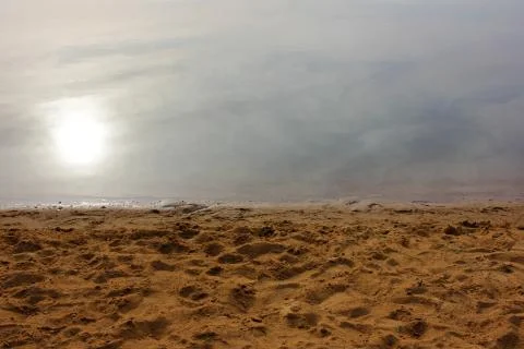Empty yellow sandy beach, dark river water, and sun reflection. Stock Photos