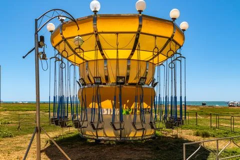 Empty yellow swing carousel on coastal grass field Stockfoto's