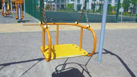 Empty yellow swing swaying on chains at sunny outdoor playground Stock Footage 340579758