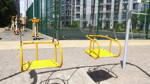 Empty yellow swing swaying on chains at sunny outdoor playground Stock Footage 340579760