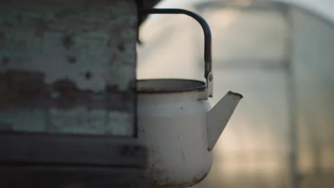 Enamel kettle in evening light. Worn kettle hanging with dusk background. Used 動画素材 348292025