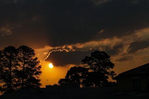 End of the day with the sun between clouds and the silhouette of trees, being Stock Photos