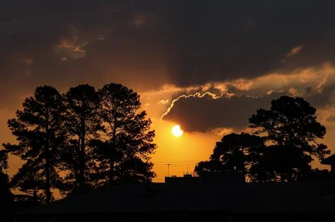 End of the day with the sun between clouds and the silhouette of trees, being Foto stock