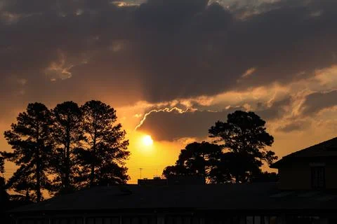 End of the day with the sun between clouds and the silhouette of trees, being Stock Photos