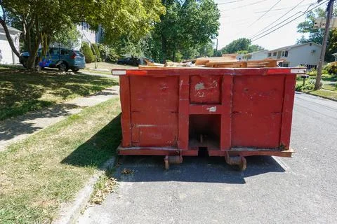 End view of a large red beat up dumpster on the street by a curb in a residen Stock Photos