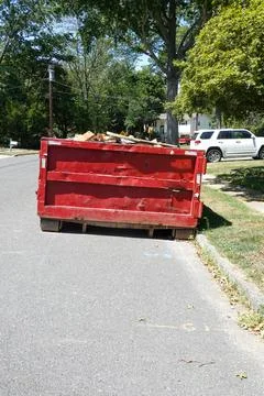 End view of a large red beat up dumpster on the street by a curb in a residen Stock Photos