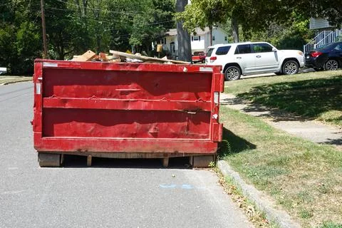 End view of a large red beat up dumpster on the street by a curb in a residen Stock Photos