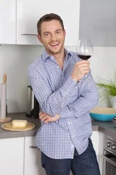 At the end of work: single man drinking glass of wine in the kitchen. Stock Photos