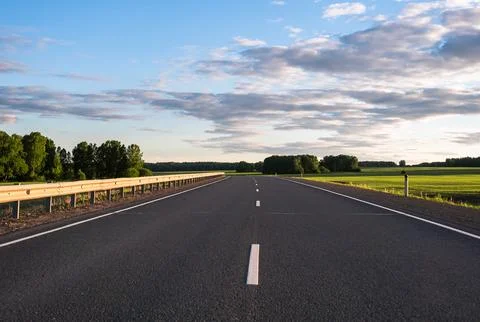 Endless asphalt road stretching through lush green fields under open blue sky Stock Photos