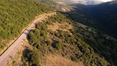 Endless straight dirt road crossing remote mountain forest at golden sunrise Stock Footage 344096229