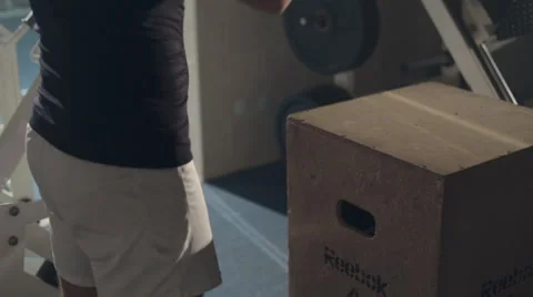 Enduring man jumps on wooden cube in the gym Stock Footage 48993494