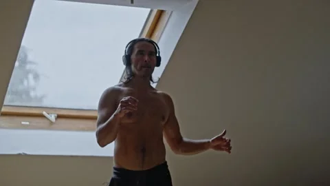 An Energetic and Enthusiastic Man Training at Home While Wearing Headphones for Stock Footage 308664129
