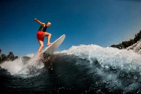 Energetic athletic man actively balancing on surf style wakeboard on splashing Stock Photos