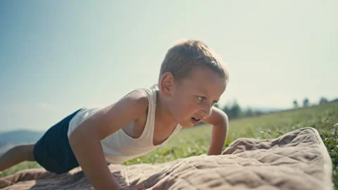 Energetic Boy Doing Pushups in Undershirt on a Blanket in nature Stock Footage 260451618
