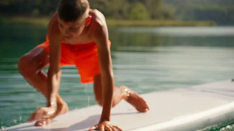 Energetic boy in orange shorts attempting to climb onto stand-up paddleboar.. Stock-Footage 317809052