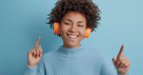 Energetic dark skinned Afro American woman listens catchy song wears stereo Stock Footage 144915120
