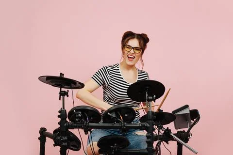 Energetic eccentric lady playing on electric drums. Over pink background. Stock Photos
