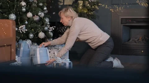 Energetic elderly woman stacking boxes with gifts under the Christmas tree Stock Footage 261181479
