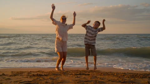 Energetic Mother and Son Dancing and Leaping with Joy on Sunset Beach Stock Footage 318393161