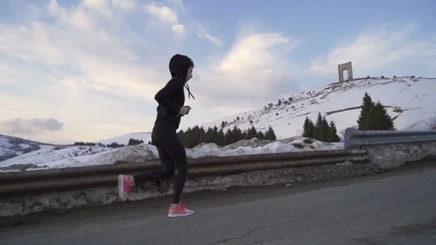 Energetic professional female runner practicing in the snowy mountains on sunset Stock Footage 125855384