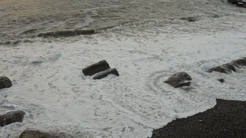 Energetic surf crashes onto jagged rocks under cloudy evening sky 動画素材 335950570