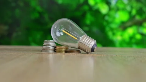 Energy saving concept with light bulb and coins on wooden table Stock Footage 332052845