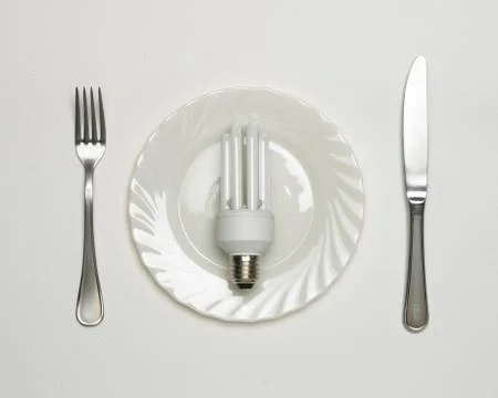 ENERGY SAVING ELECTRIC LIGHT BULB ON WHITE PLATE WITH KNIFE AND FORK Stock Photos