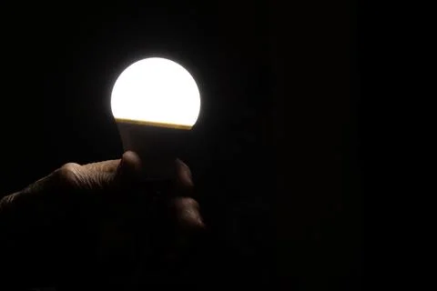 Energy saving light bulb in hand of elderly woman in dark room Stock Photos