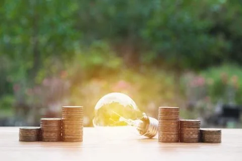 Energy saving light bulb with stacks of coins on nature background. Stock Photos