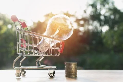 Energy saving light bulb with stacks of coins and shopping cart for saving, f Stock Photos