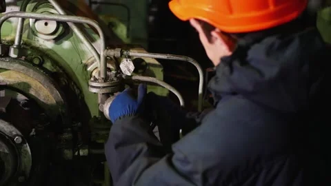 An energy worker in an orange hardhat and uniform turns a pipeline valve Stock Footage 169518404