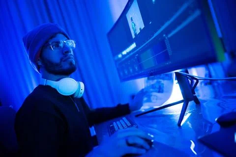Engaged content creator working on video editing in a stylish blue-lit work.. Stock Photos