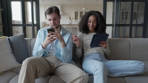 Engaged Couple Sharing Content, Discussing Tablet Screen Sitting Comfortably Видео 303759108