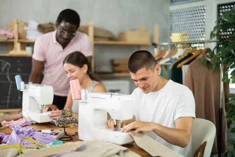 Engaged guy stitching fabric on machine in sewing class for adults 스톡 사진