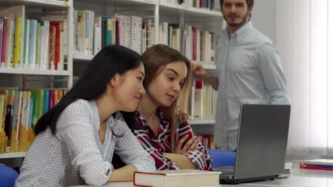 Engaged students collaborating on a laptop in a vibrant library Stock Footage 311991974