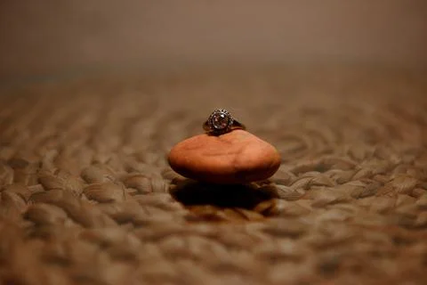 Engagement ring displayed on smooth stone with woven background Stock Photos