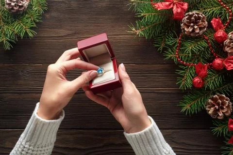 Engagement ring in female hands among Christmas decorations on wood background Foto stock