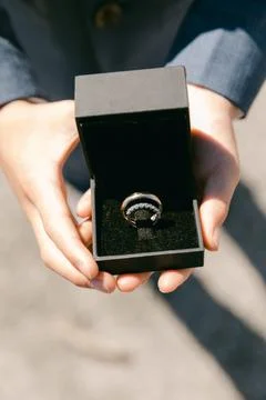 Engagement ring presented in a black box held by hands during a bright outdoor Stock Photos