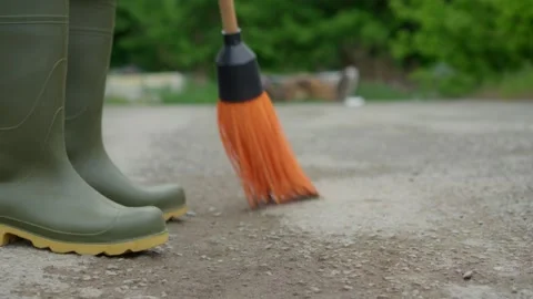 Engaging in the activity of sweeping the ground while wearing green rubber boots Stock Footage 309421806