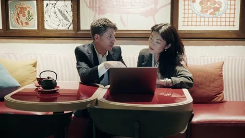 Engaging conversation between two young professionals at a cafe with a laptop Vidéo 304540616